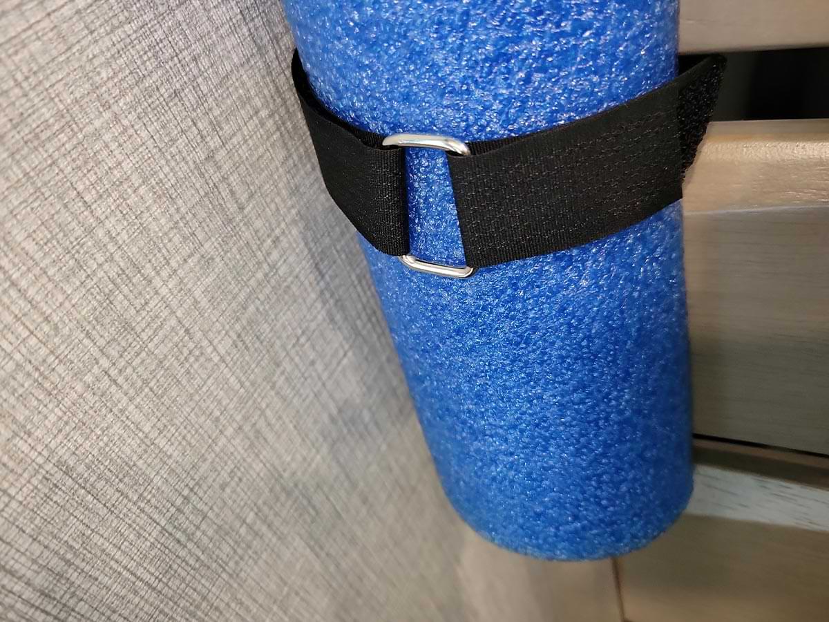 close view of a nylon strap with a buckle ring holding a swim noodle piece snugly to a dinette chair back