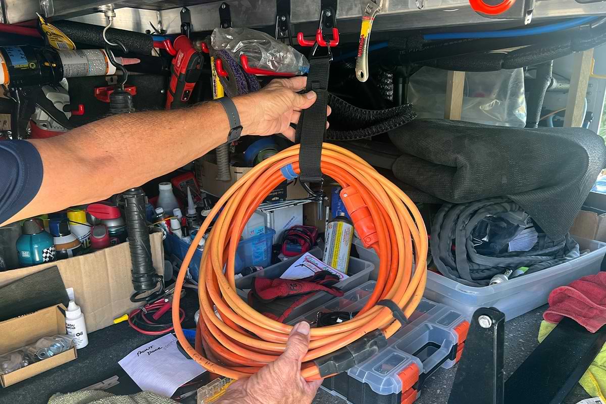 an Extension Cord Organizer strap is wrapped around a long orange power extension cord roll and hung in an external RV storage compartment