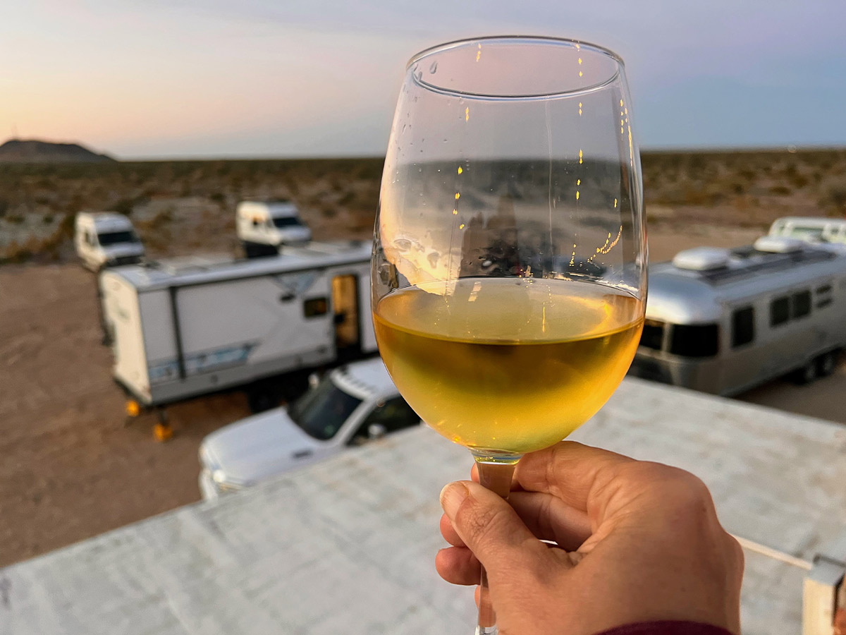 close view of a hand holding a glass of chilled wine, out of focus in the background are many parked RVs and camper vans