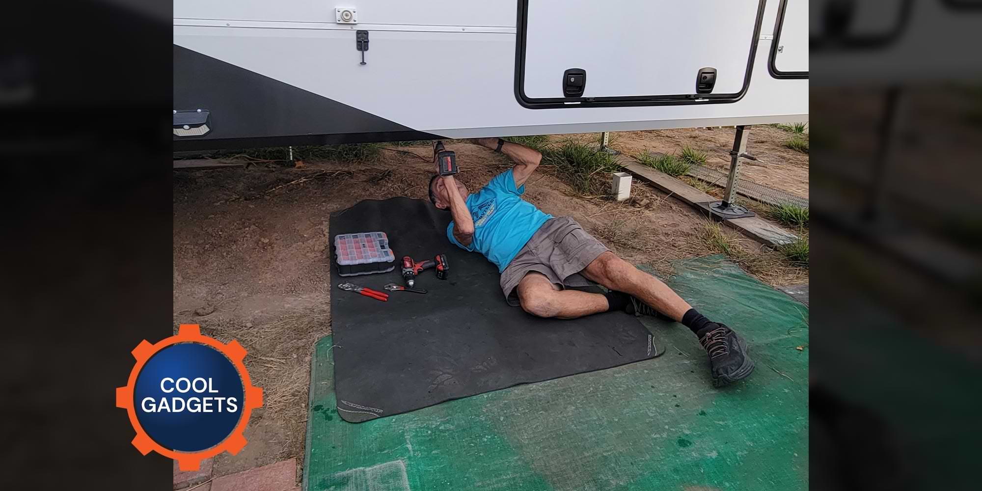 a man lays on a large black mat while working beneath an RV