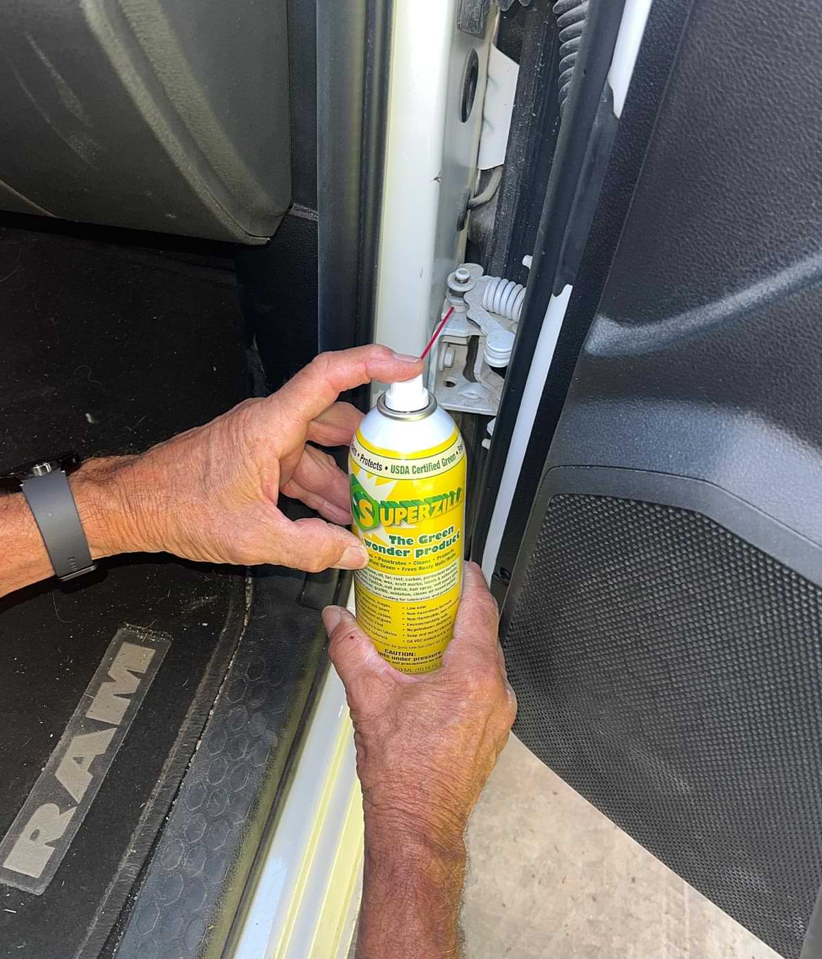 hands spray Superzilla on a cab door hinge of a Ram 3500 pickup