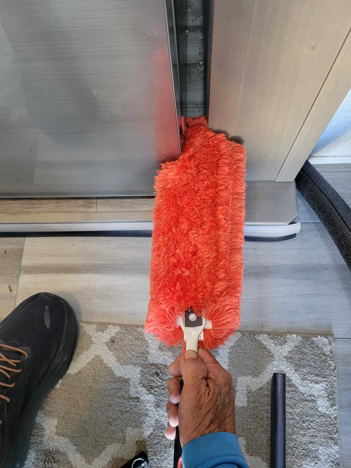 a bright red dusting brush is used to clean the gap to the side of the RV refrigerator but the brush doesn't cover the length of the gap