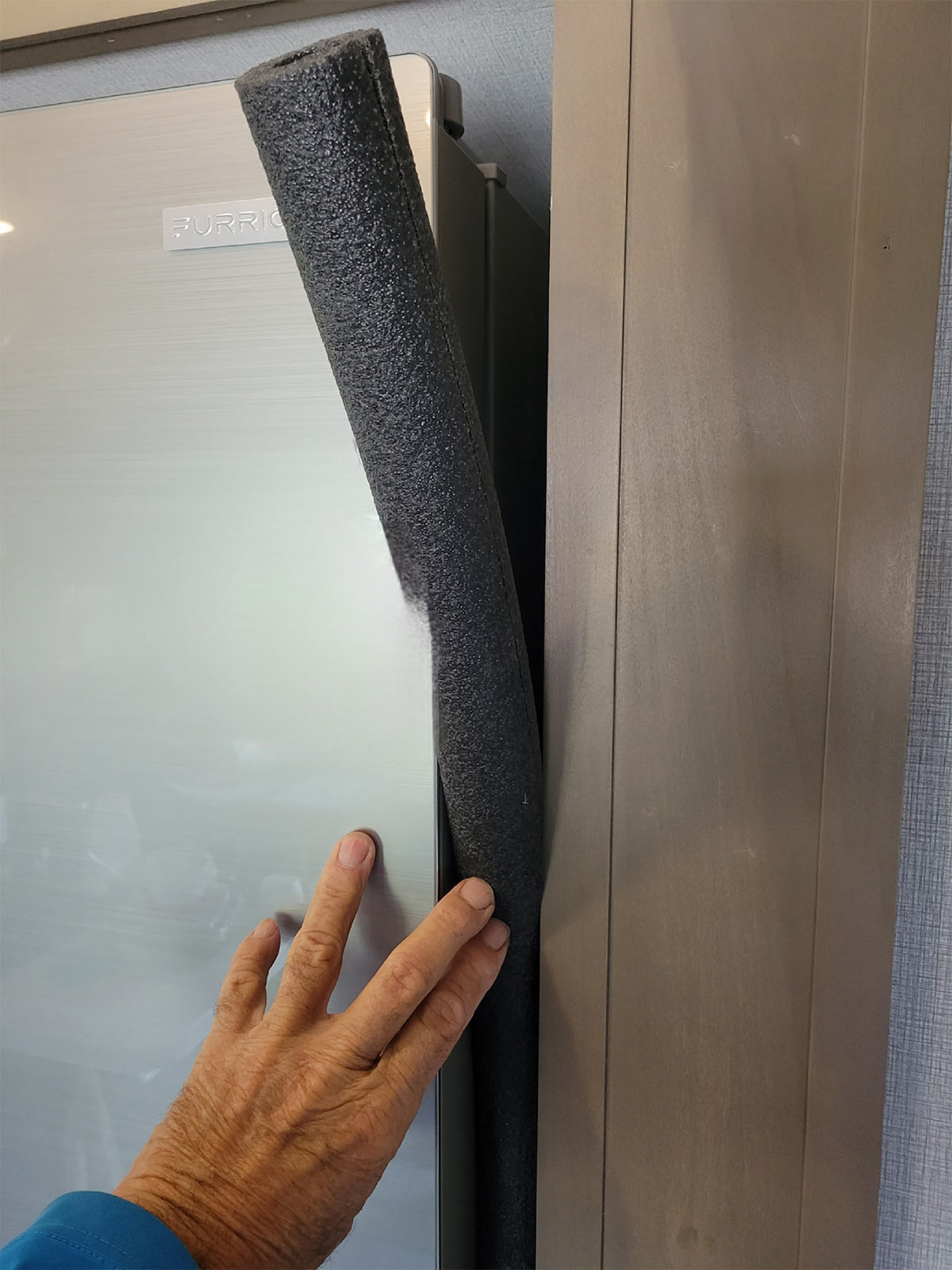 a hand places the foam insulation between the refrigerator and cabinet walls