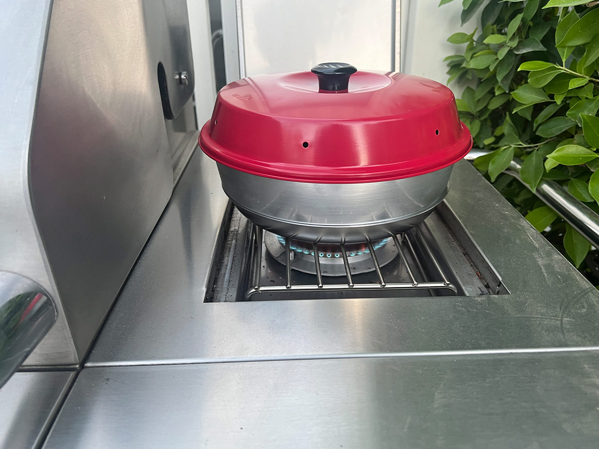 Omnia Stovetop Oven kit sits over a operating burner on the side of a barbecue
