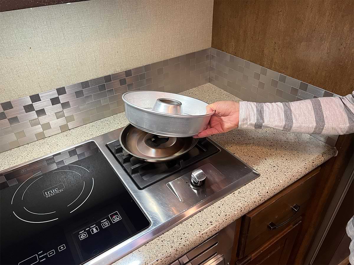 a hand holds the Omnia bowl over a gas cooktop connected to a larger induction cooktop in an RV kitchen