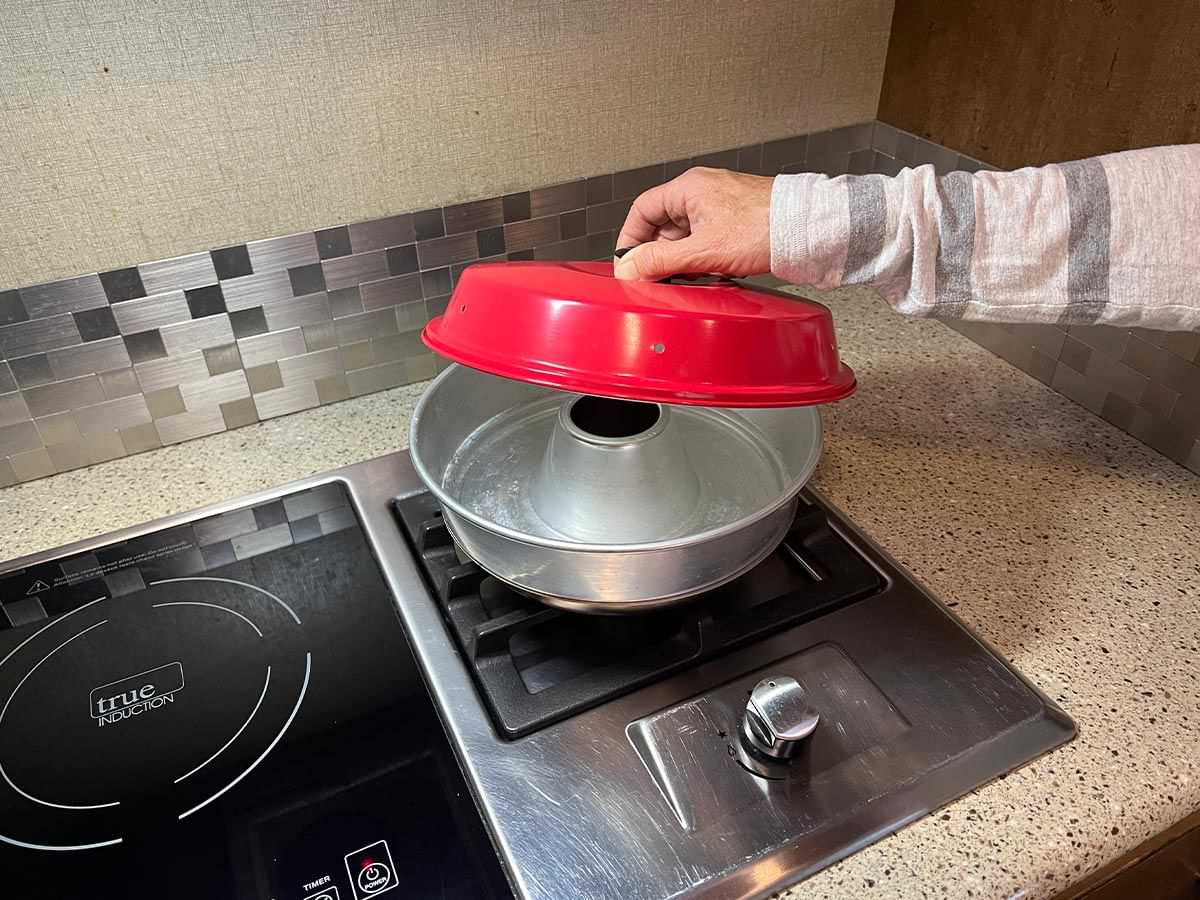 a hand holds the Omnia ventilated lid over the Omnia bowl on the kitchen gas cooktop