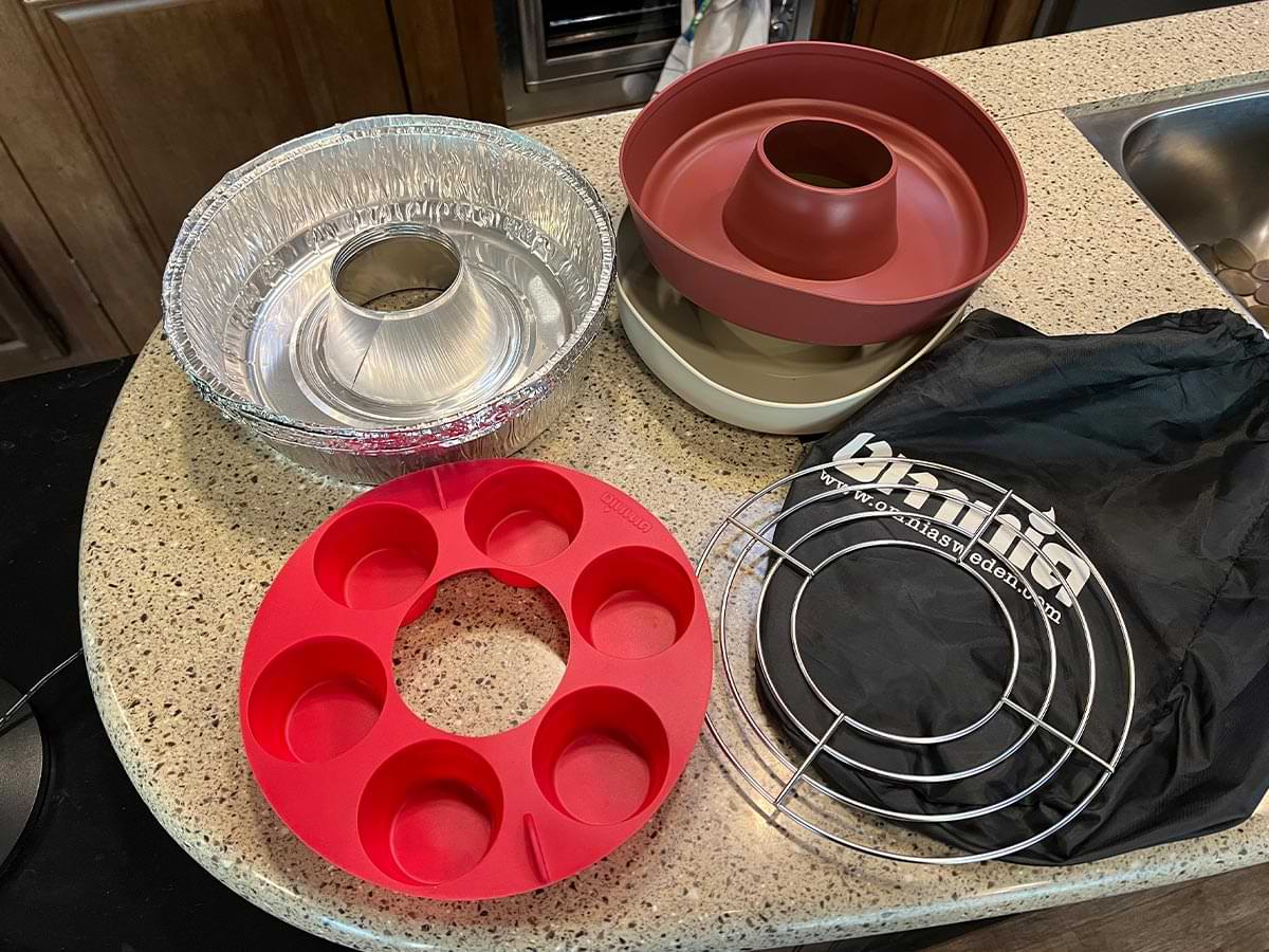 the Omnia Stovetop Oven kit parts layed out on a kitchen counter including silicone molds and foil baking molds