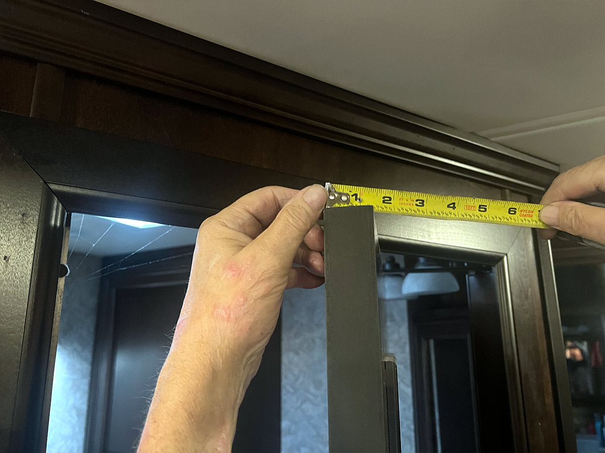 hands use a measuring tape to determine the width of the top of a door