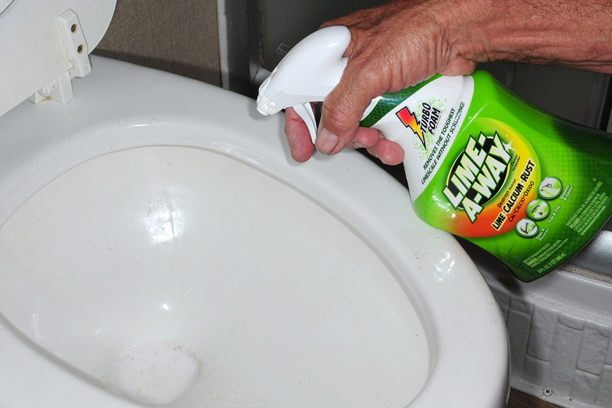 a hand sprays Lime-A-Way into an RV toilet bowl