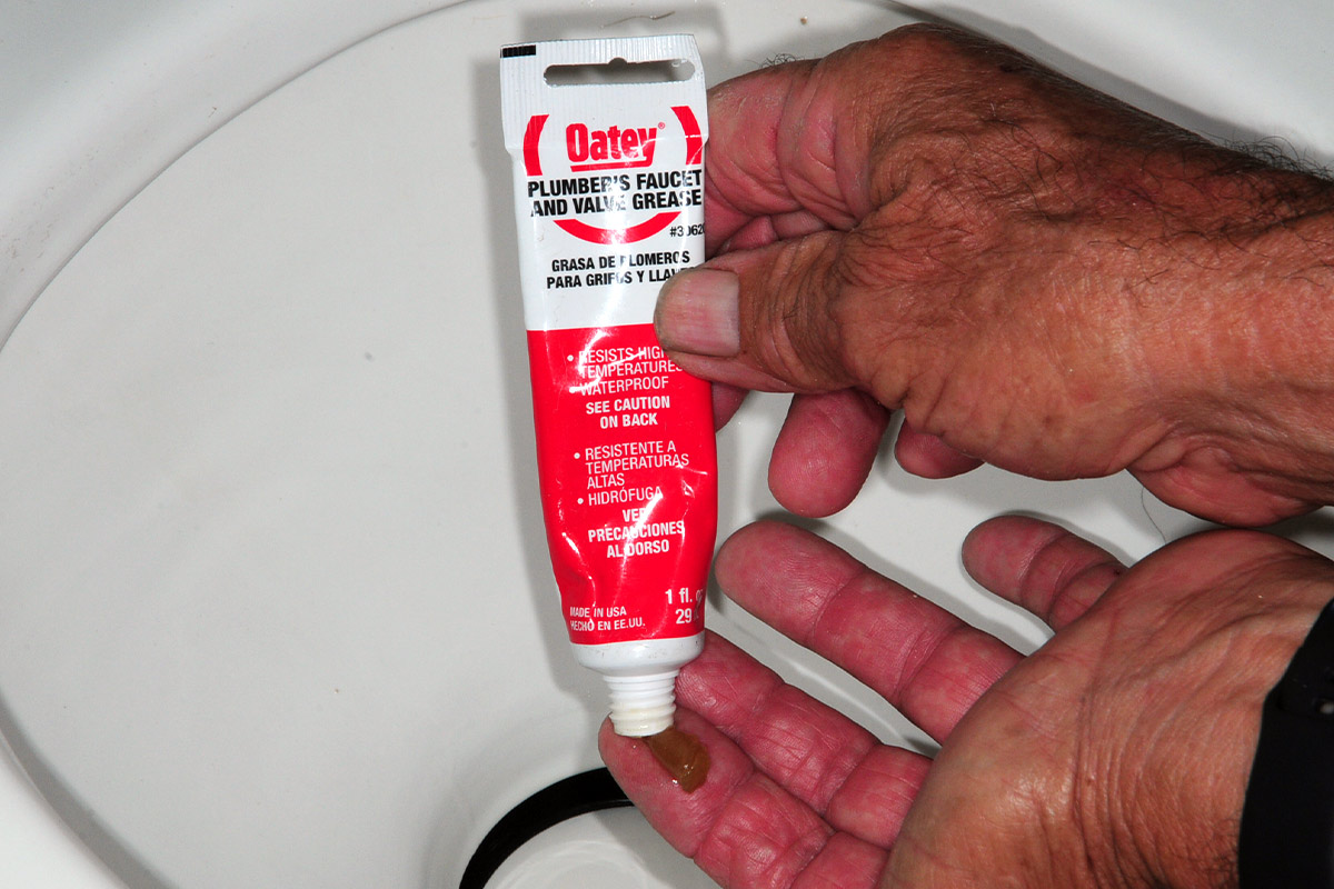 a hand holding a tube of Oatey Plumber’s Faucet and Valve Grease squeezes a small gob onto an index finger