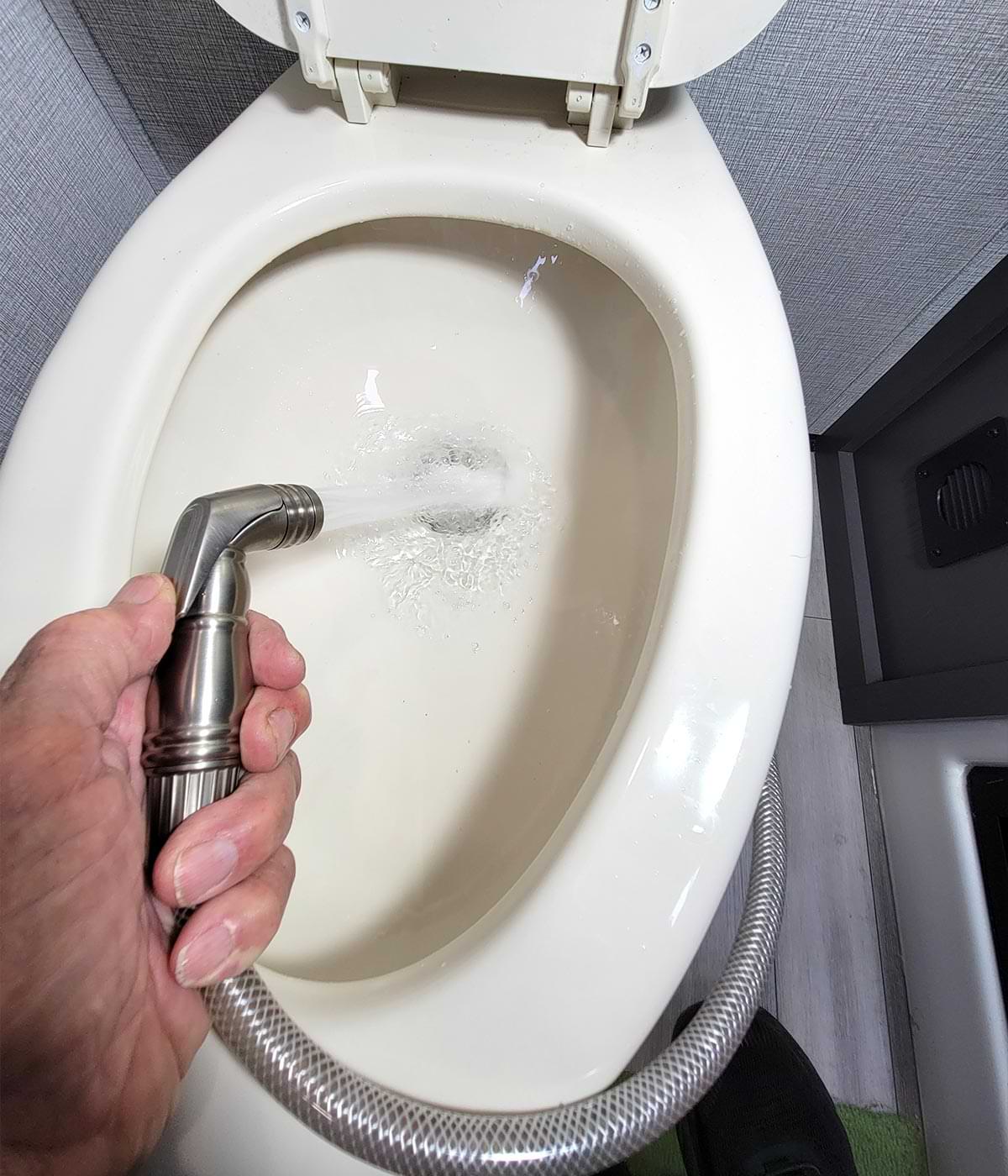 close top view of a hand spraying the installed head into the RV toilet