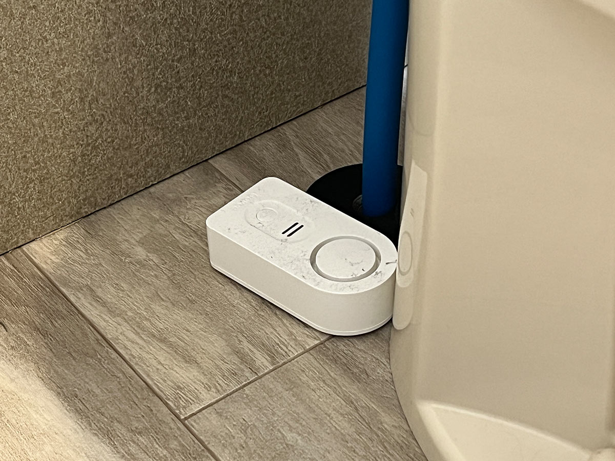 close view of a Govee water alarm sensor placed beside a water pipe to the toilet