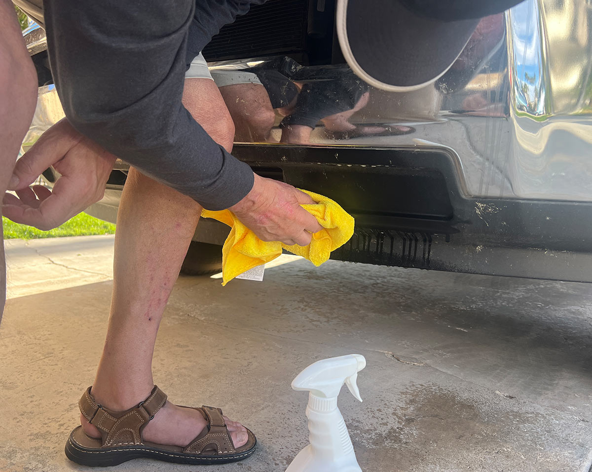a yellow microfiber towel is used to clean the dead bug splatter from the vehicle bumper