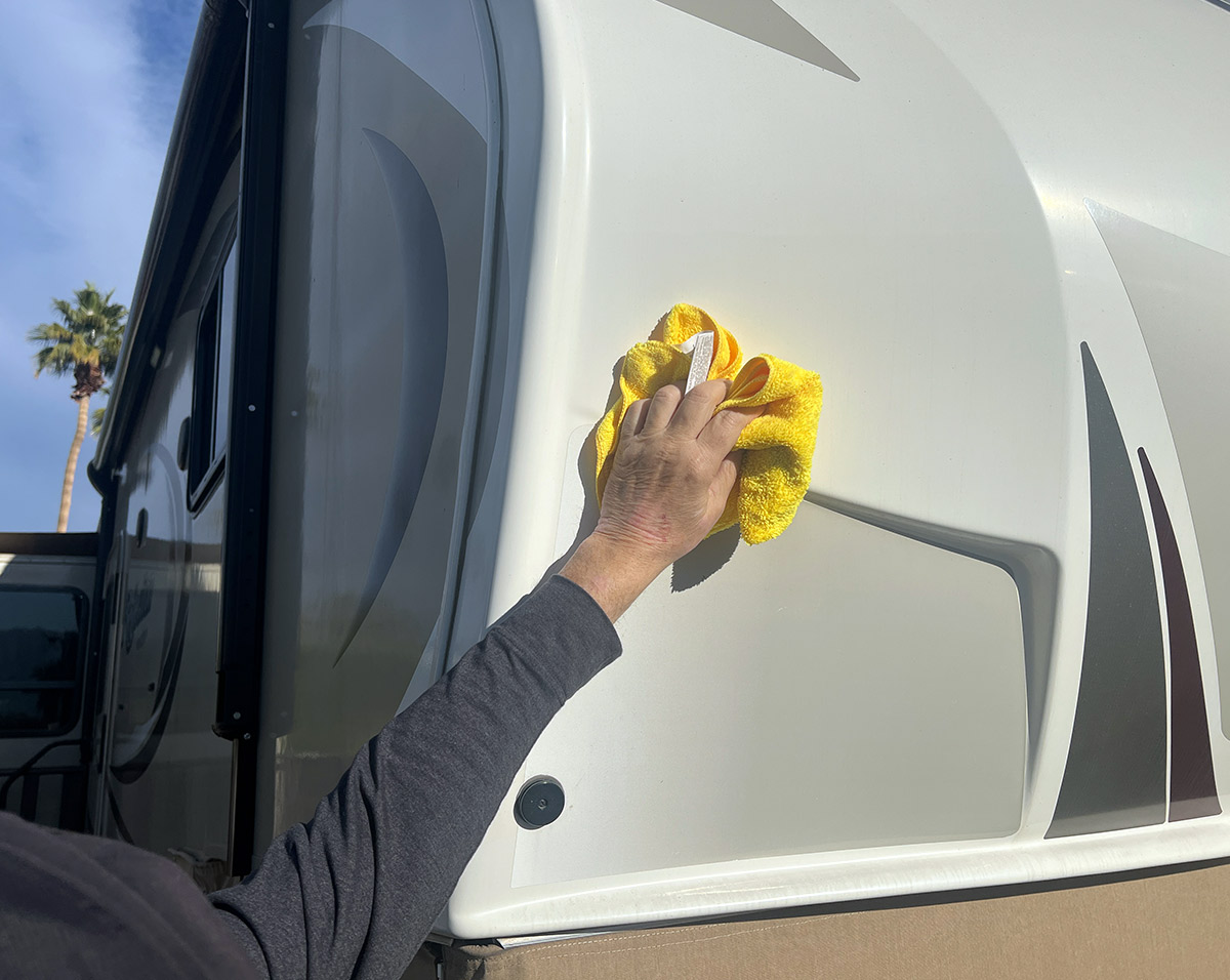 a hand uses a microfiber towel to wipe an exterior side of an RV