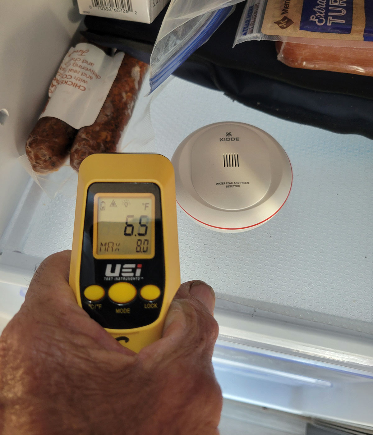 the Kidde disc sits on a shelf in a refrigerator, a hand holds a temperature gun to measure the temperature of the refrigerator