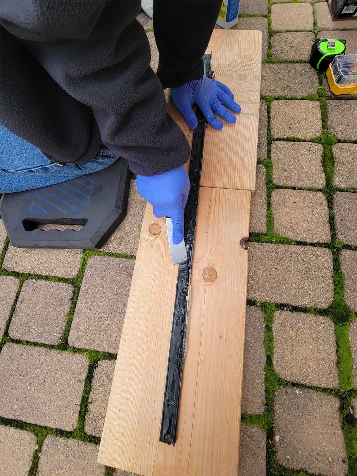 using a putty knife and pieces of wood as a base, gloved hands remove the remaining putty from the molding