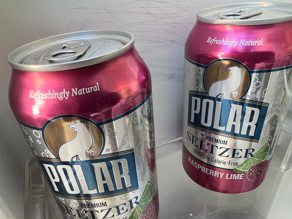 close view of two Seltzer cans in a refrigerator door compartment, behing the cans a gray scratch marks on the refrigerator wall