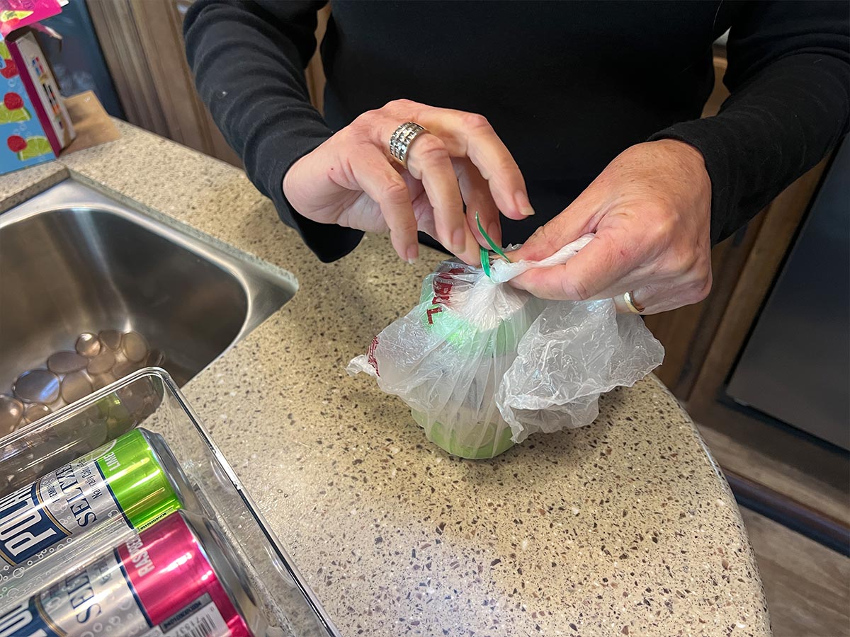a woman's hands wrap a twist tie around the opening of a produce bag holding a beverage can