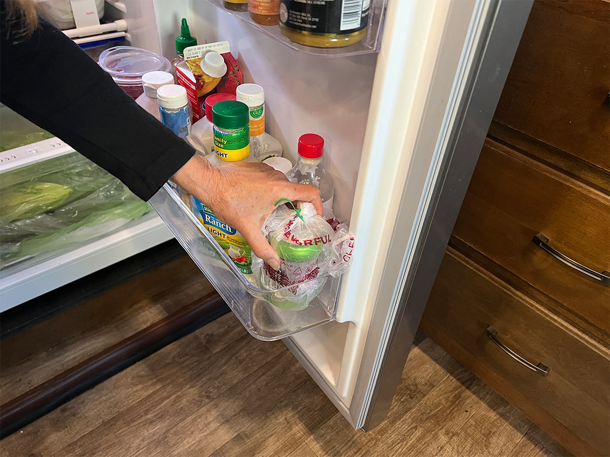 the woman's hand places the bagged beverage can in the door compartment of a refrigerator