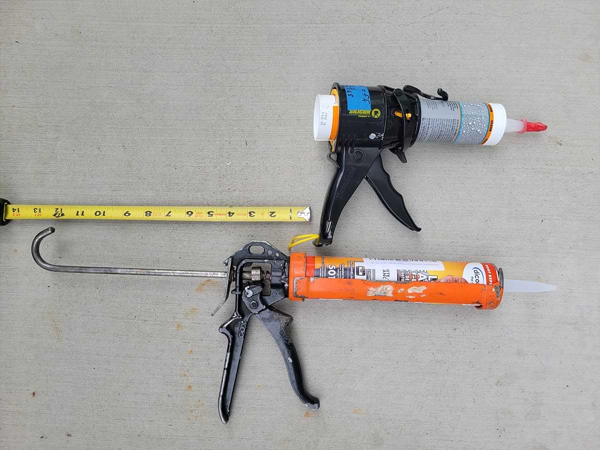 top view of a siligun placed beside a caulking gun for comparison, a measuring tape is placed along the length of the caulking gun starting from the cartridge holder base to the end of the hooked centre-rod