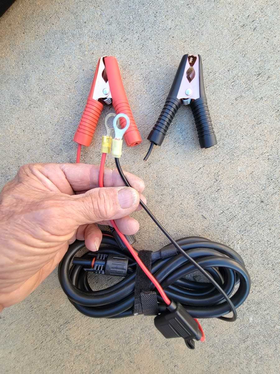 top view of a hand holding cable wire ends with ring terminals installed as a two red and black alligator clips sit to the side 