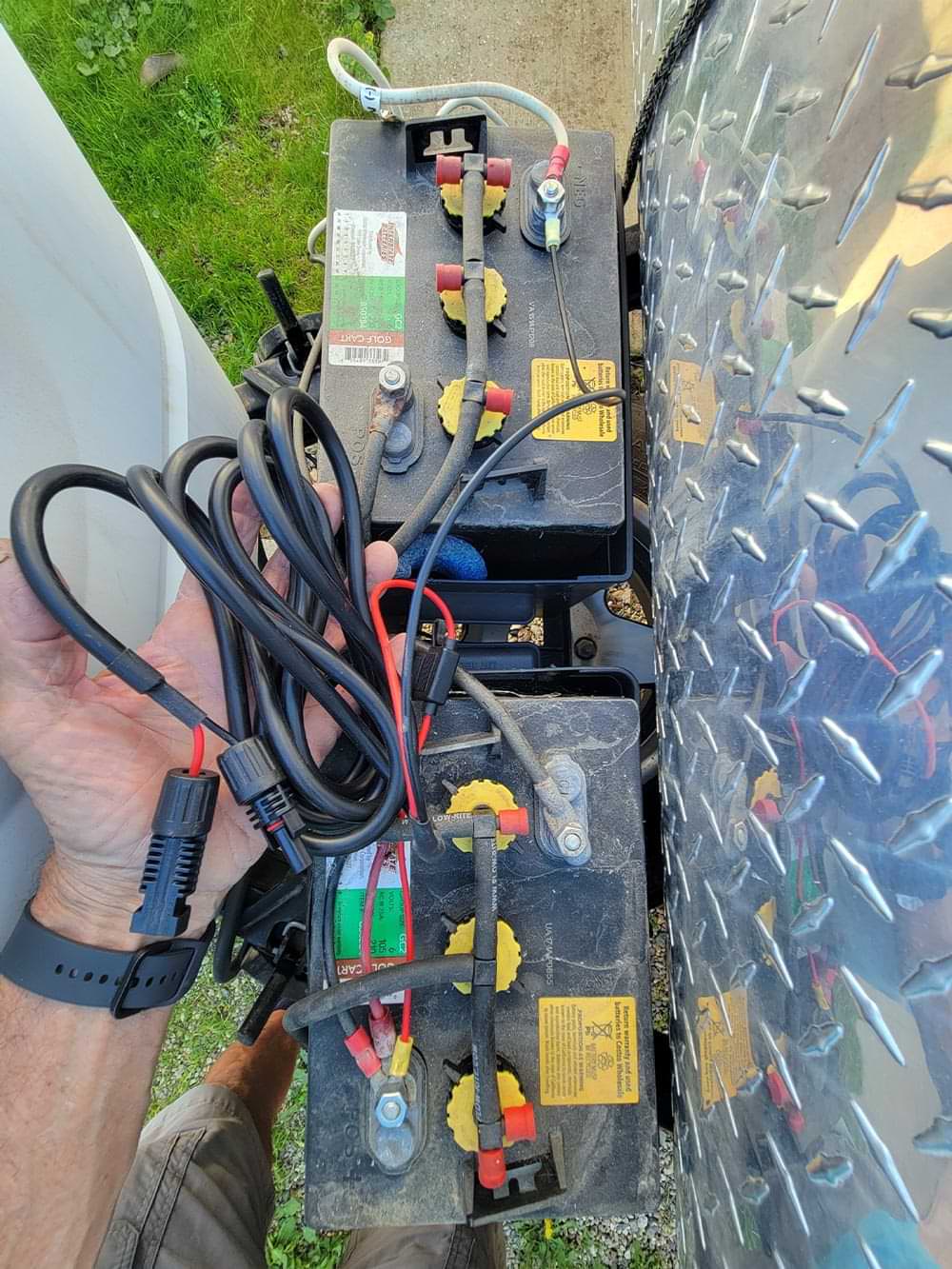a hand holds a wire from the Renogy solar panel case as it is connected to the trailer's battery