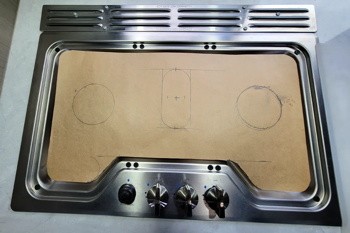 top view of a piece of craft paper on a cooktop, on the paper are markings for trimming holes