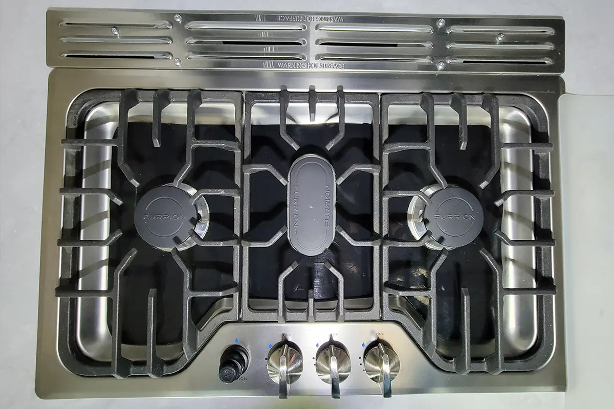 top view of the RV cooktop with its base covered by a silicone barbecue mat and the burner grates back in place
