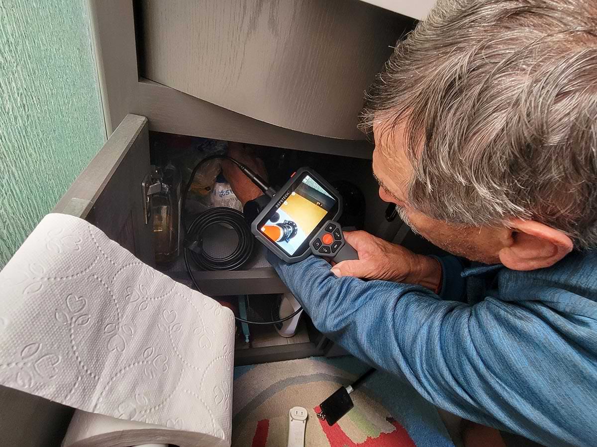 a man uses the Depstech DS590 endoscope to look at the base of a pipe in a small under sink compartment in an RV