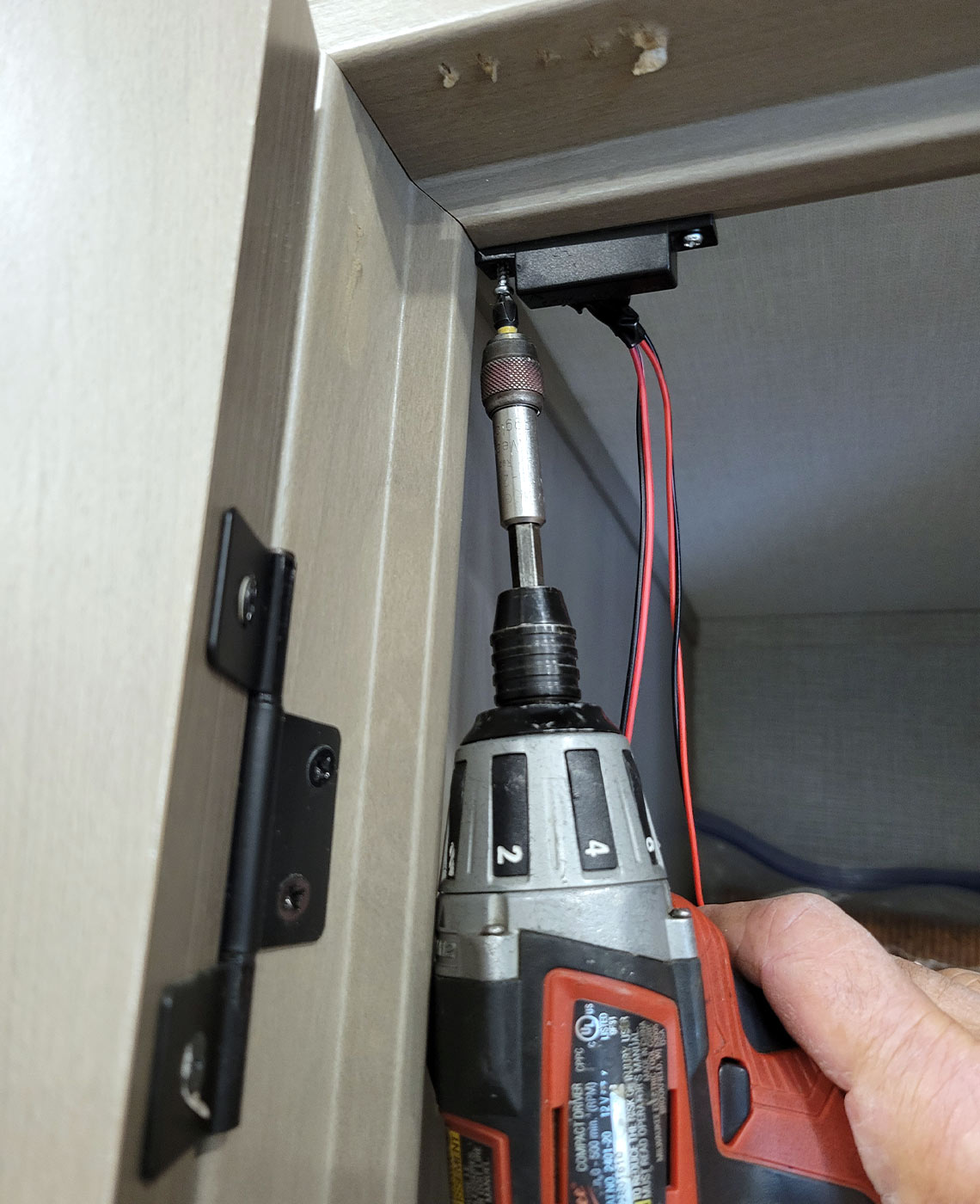 close view of the wired half of the reed switch being mounted to the pantry-door frame using a drill gun