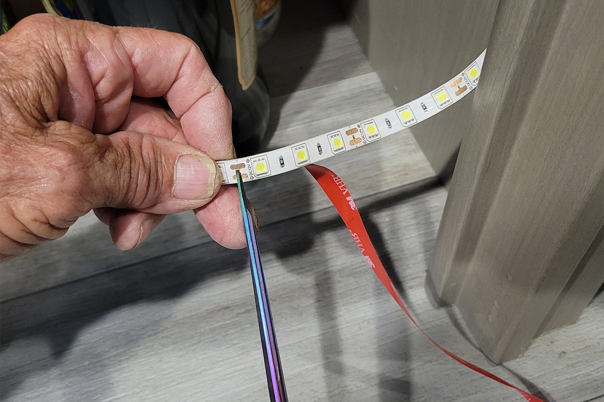close view of the LED light strip being cut at the marked point with scissors