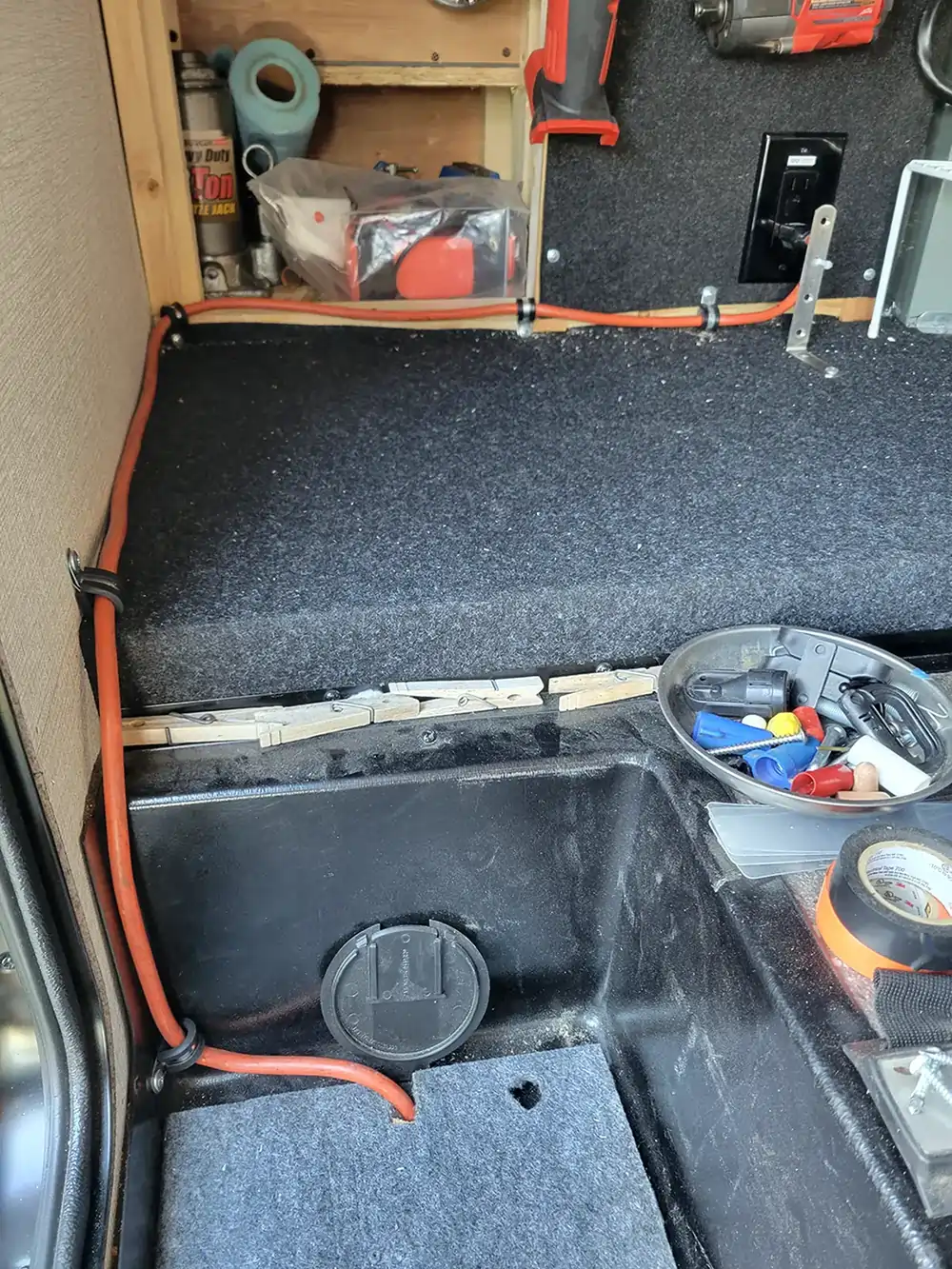 view inside the pass-through compartment of the RV, made empty for installation and showing the cable routed through the hatch and clamped to walls as it leads to the receptacle provided by the manufacturer