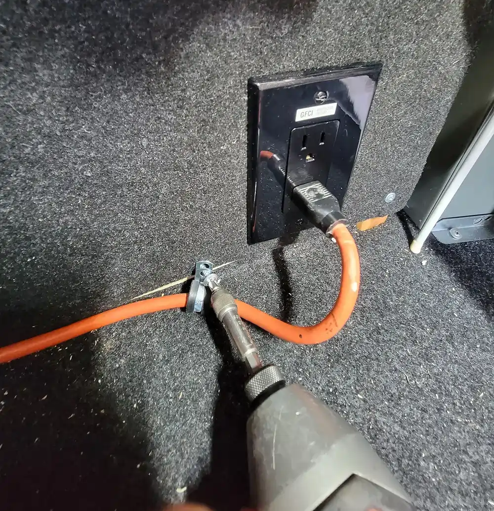 close view of a drill gun tightening the screw on a 3/8-inch clamp securing the extension cord just below the manufacturer receptacle