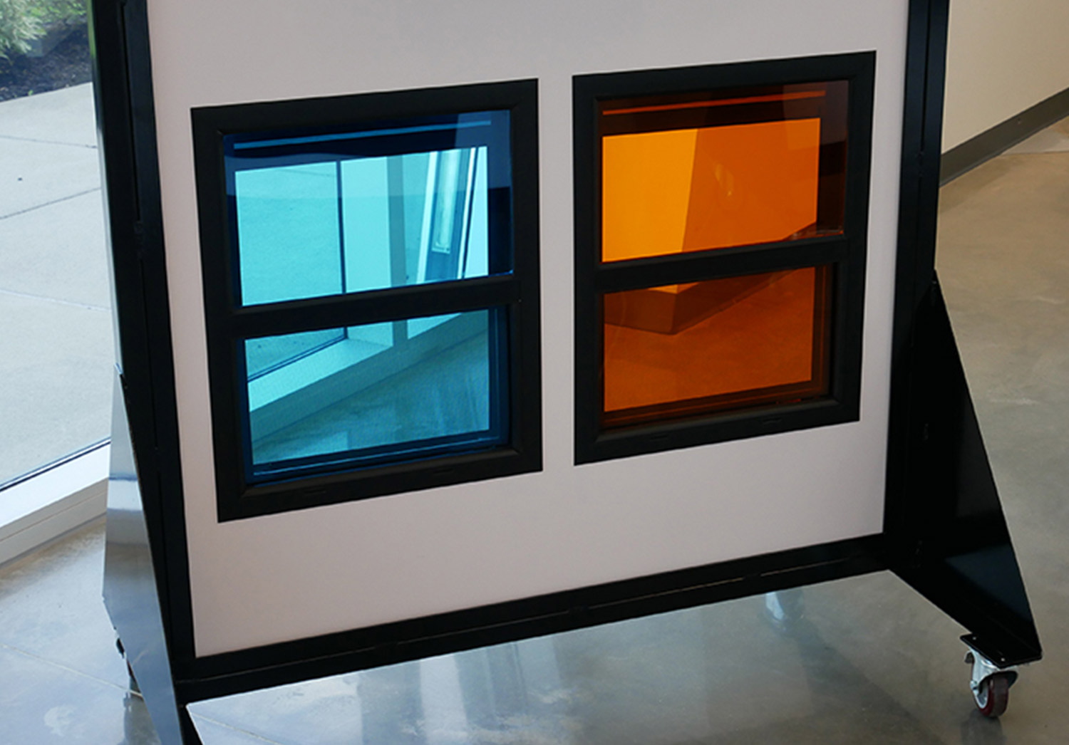 a rolling display that features two Lippert designed automotive-style square frameless windows, one with blue glass and another with orange glass
