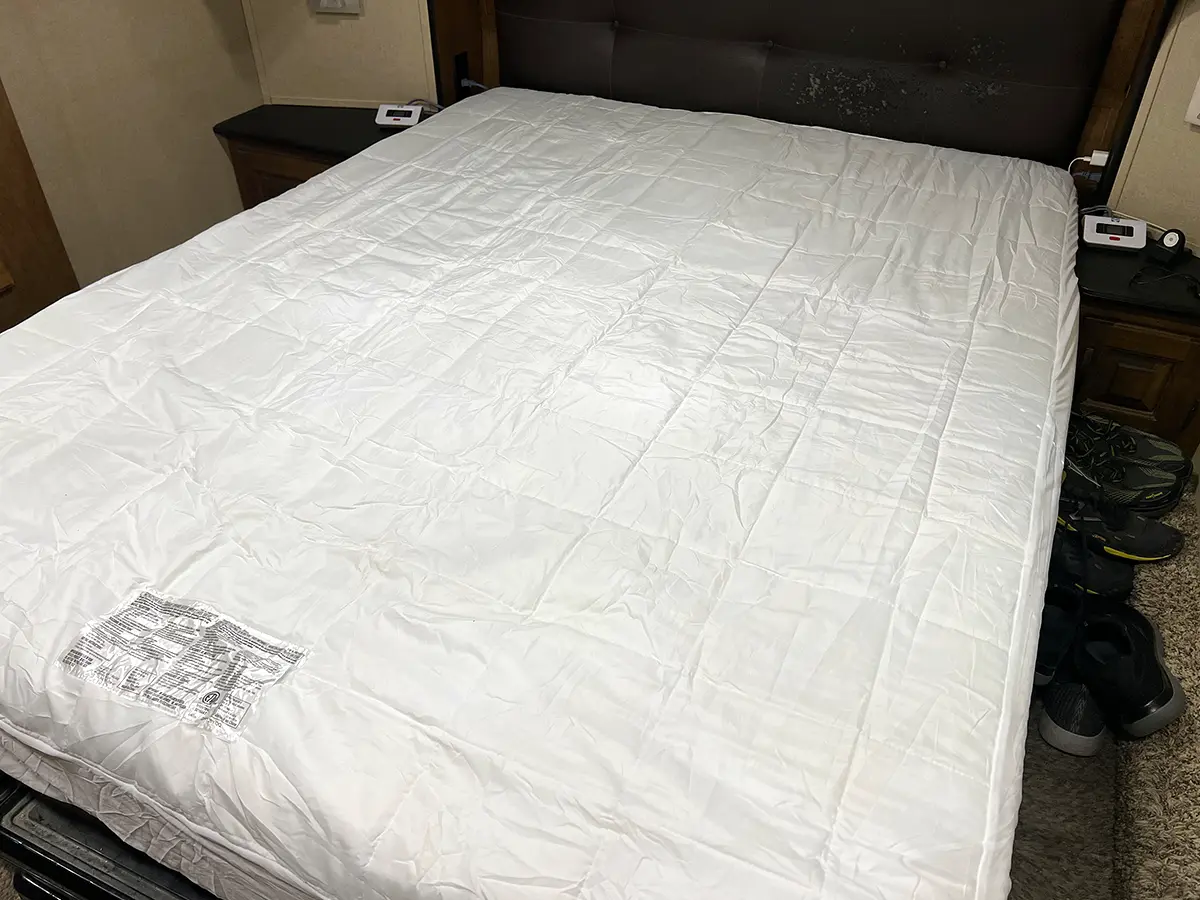 full view of the Sealy mattress heating pad on an RV master bed, the controllers for either side of the pad rest on night stands on either side of the bed