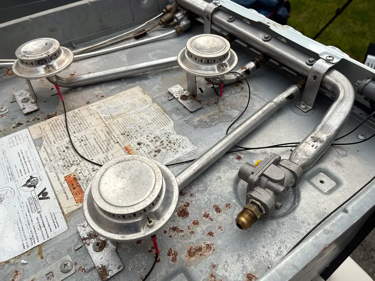 angled view of an RV range with its propane gas line and other valves visible