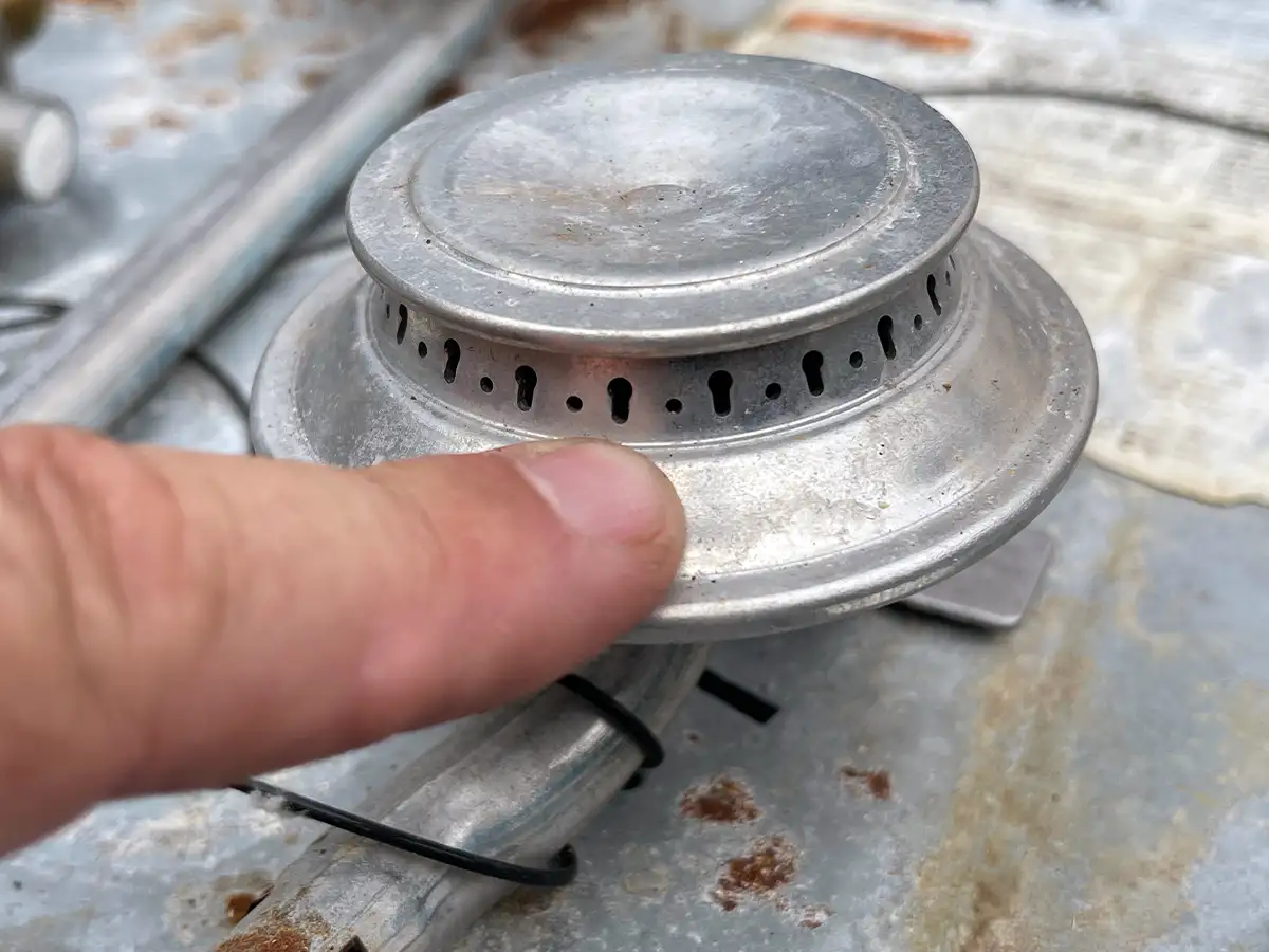 close view of an index finger pointing to the ports on a cooktop burner head