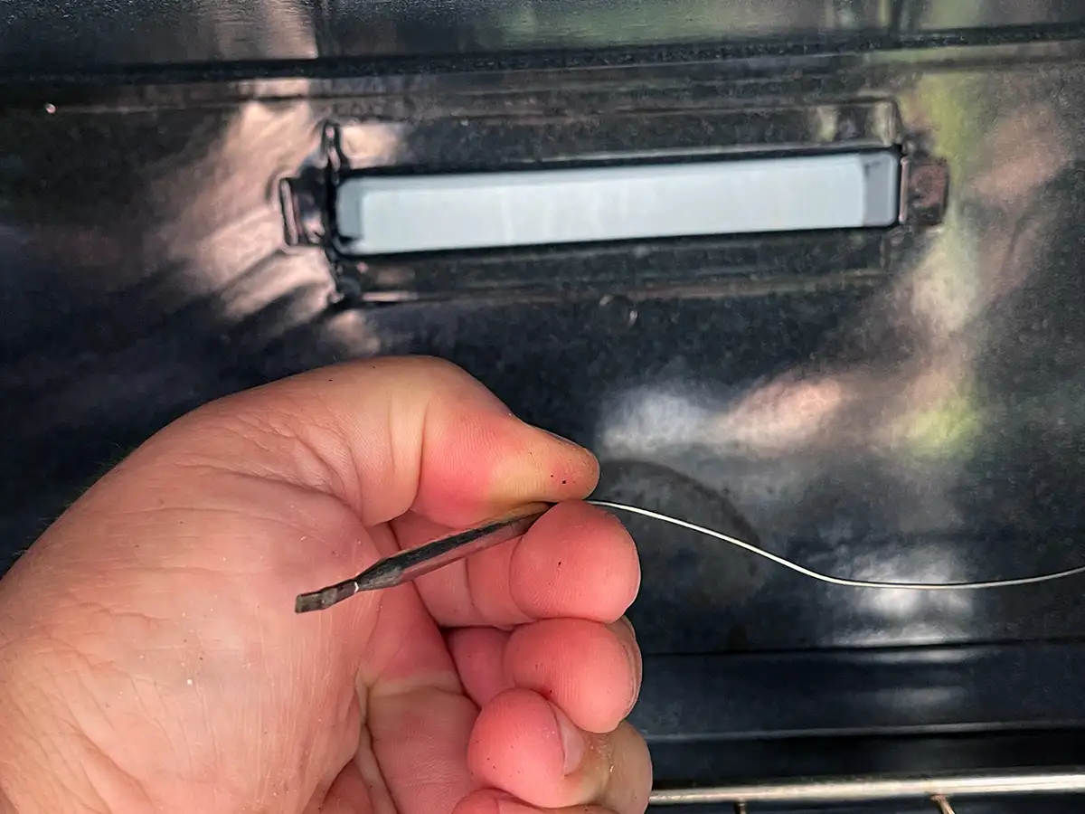 close up of a hand holding the bracket end for the oven bulb