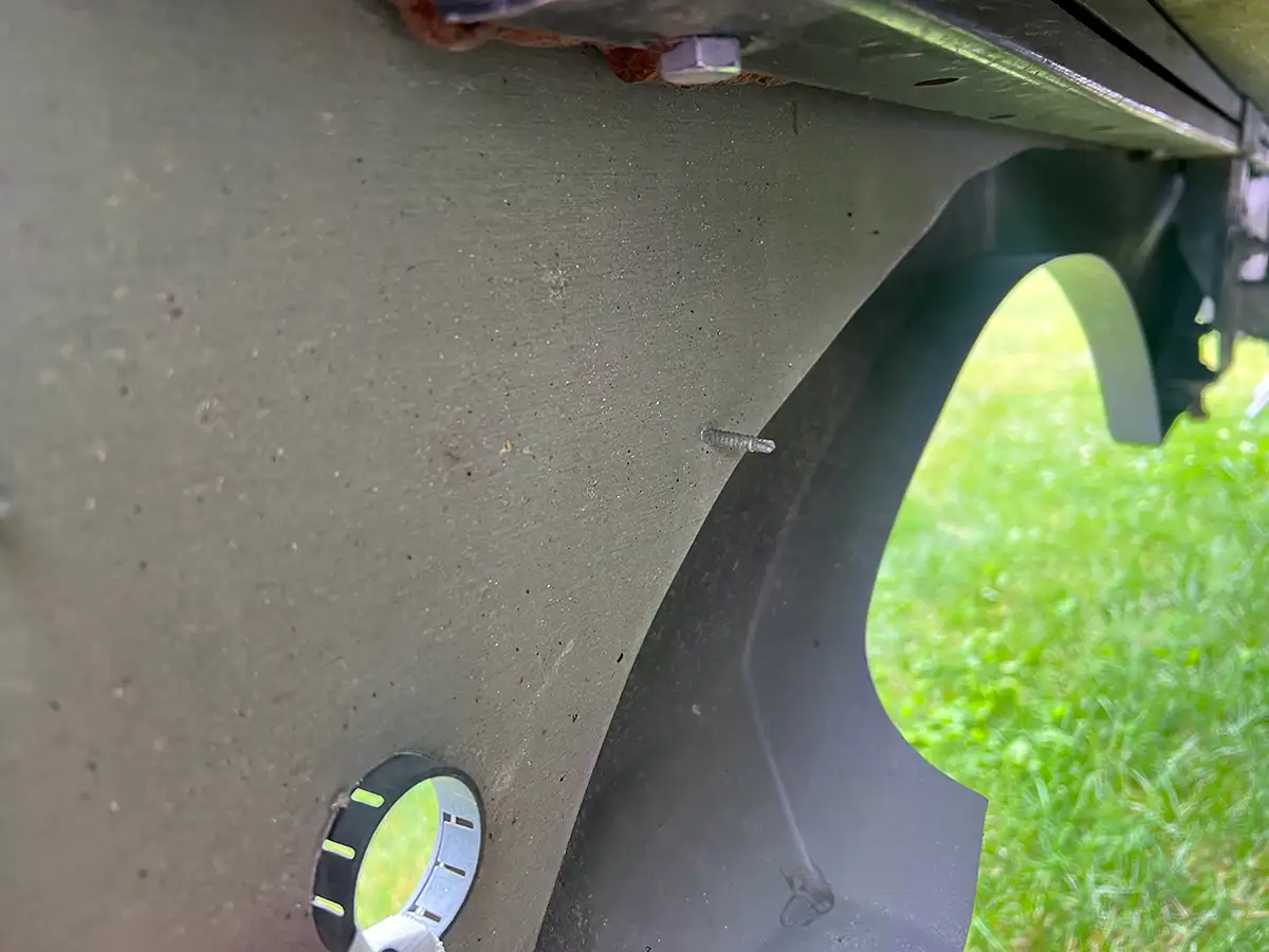 interior view of the RV undercarriage showing a factory self-drilling screw drilled in from the exterior side and attaching the fender skirt to the lower section of the slide-out