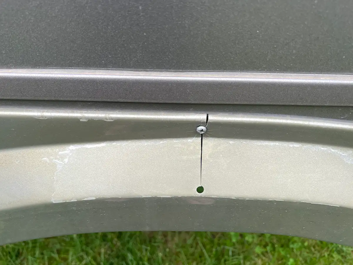 close view of a gray fender skirt, a crack runs vertically down from a self-drilling screw and ends at a drilled hole about and inch and a half below