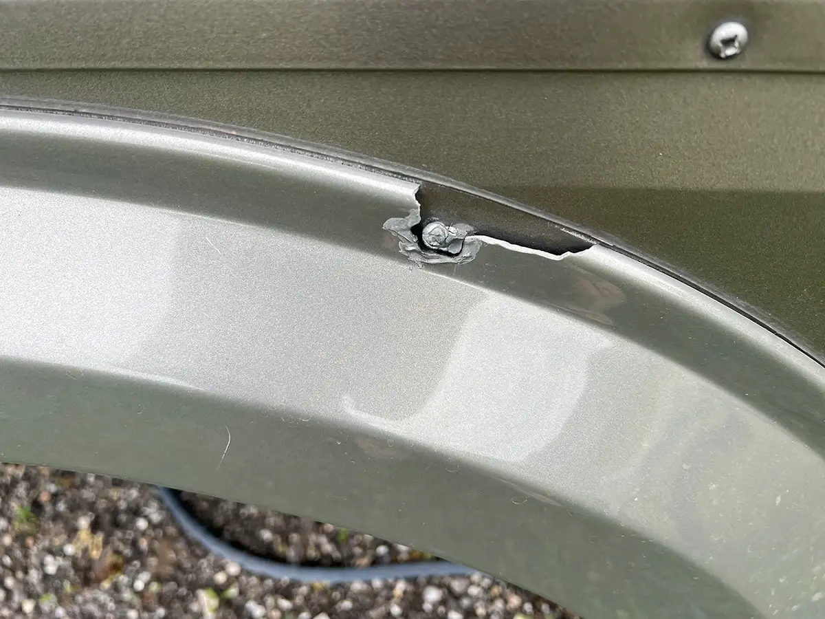 close view of a gray fender with a failed area of repair and fender skirt pieces missing