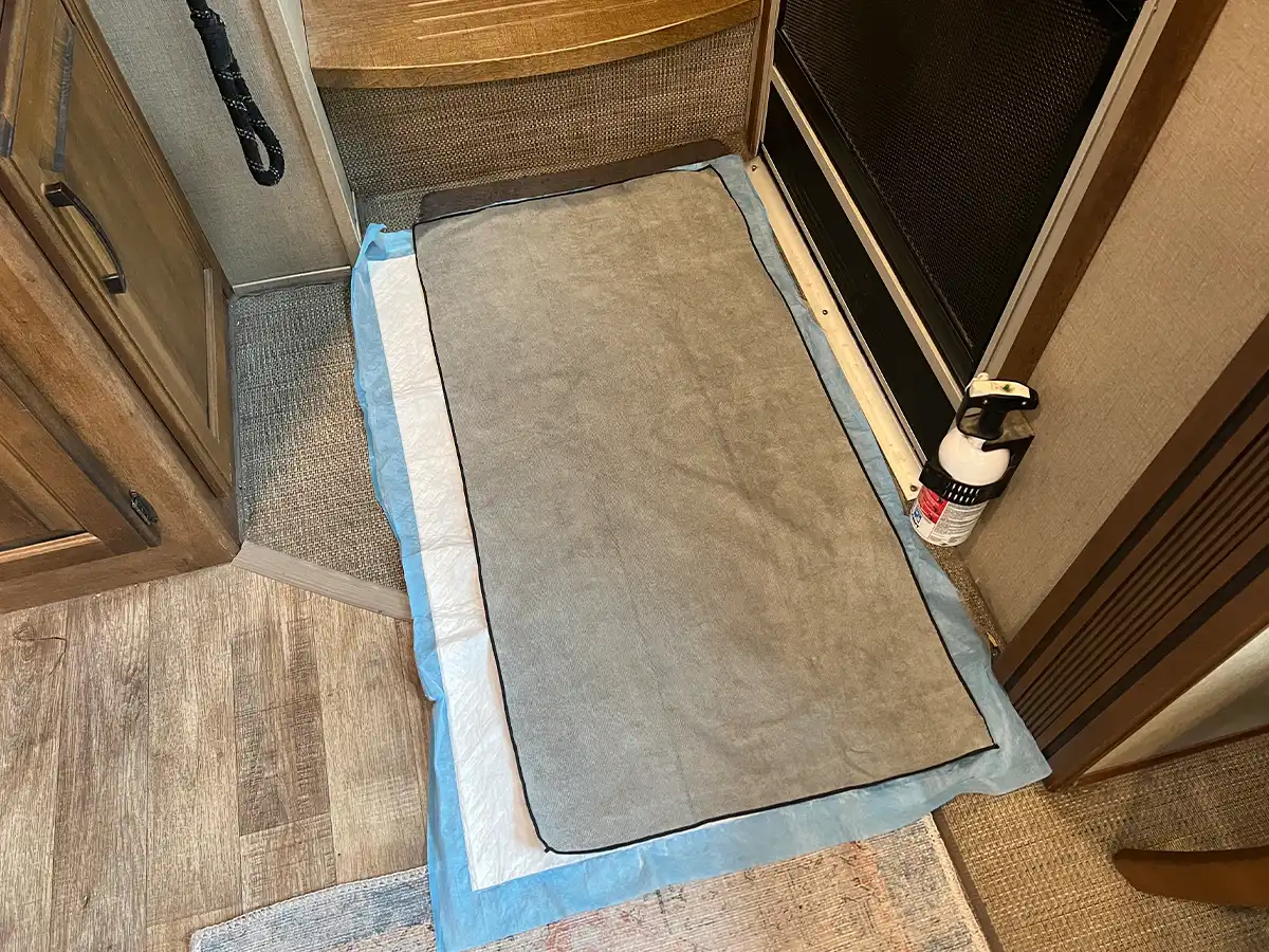 downward view at the microfiber towel and a doggy piddle pad beneath it, placed on the floor over the existing mat next to the door threshold