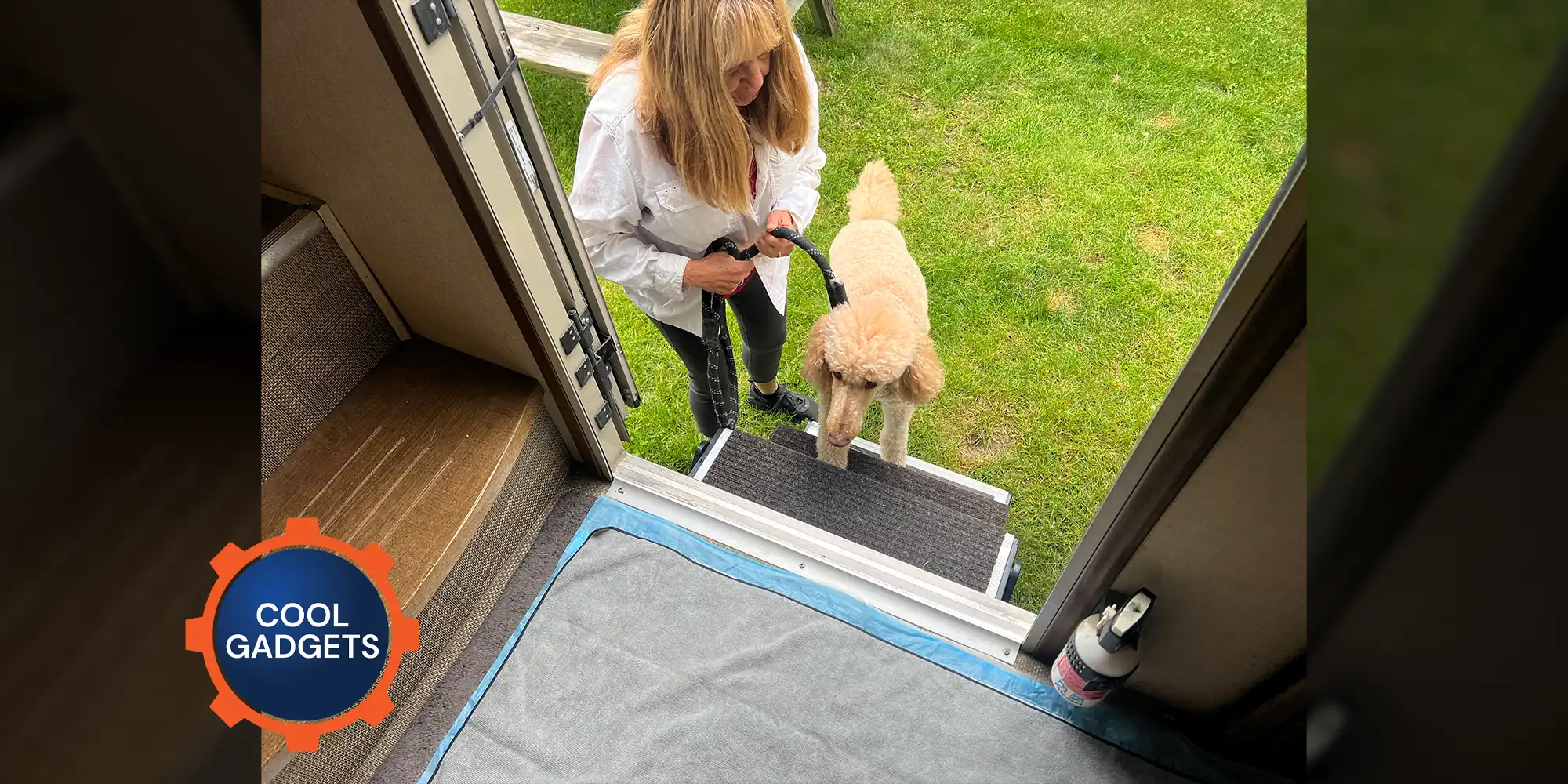 a woman holds a leash fastened to a full size blonde standard poodle as they both go up the entry steps of an RV parked on grass