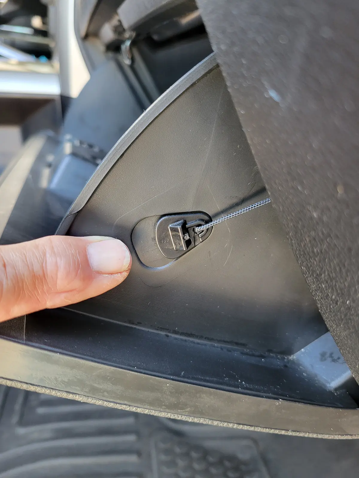 close view of a finger pointing to a spring-loaded cable that controls the movement of the glove box