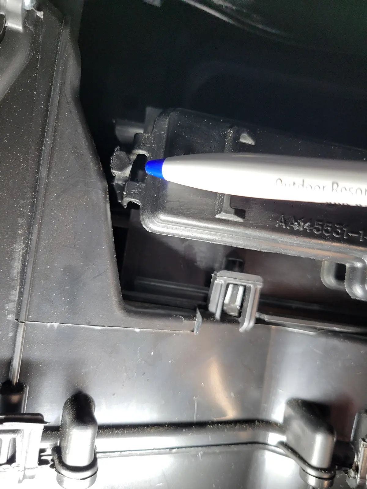 a pen is used to point to a small tab that gives access to the cabin-air-filter box