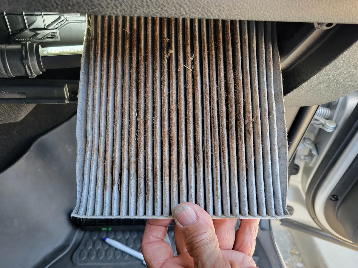 a hand holds up the old cabin air filter, showing all the crud that has built up over time