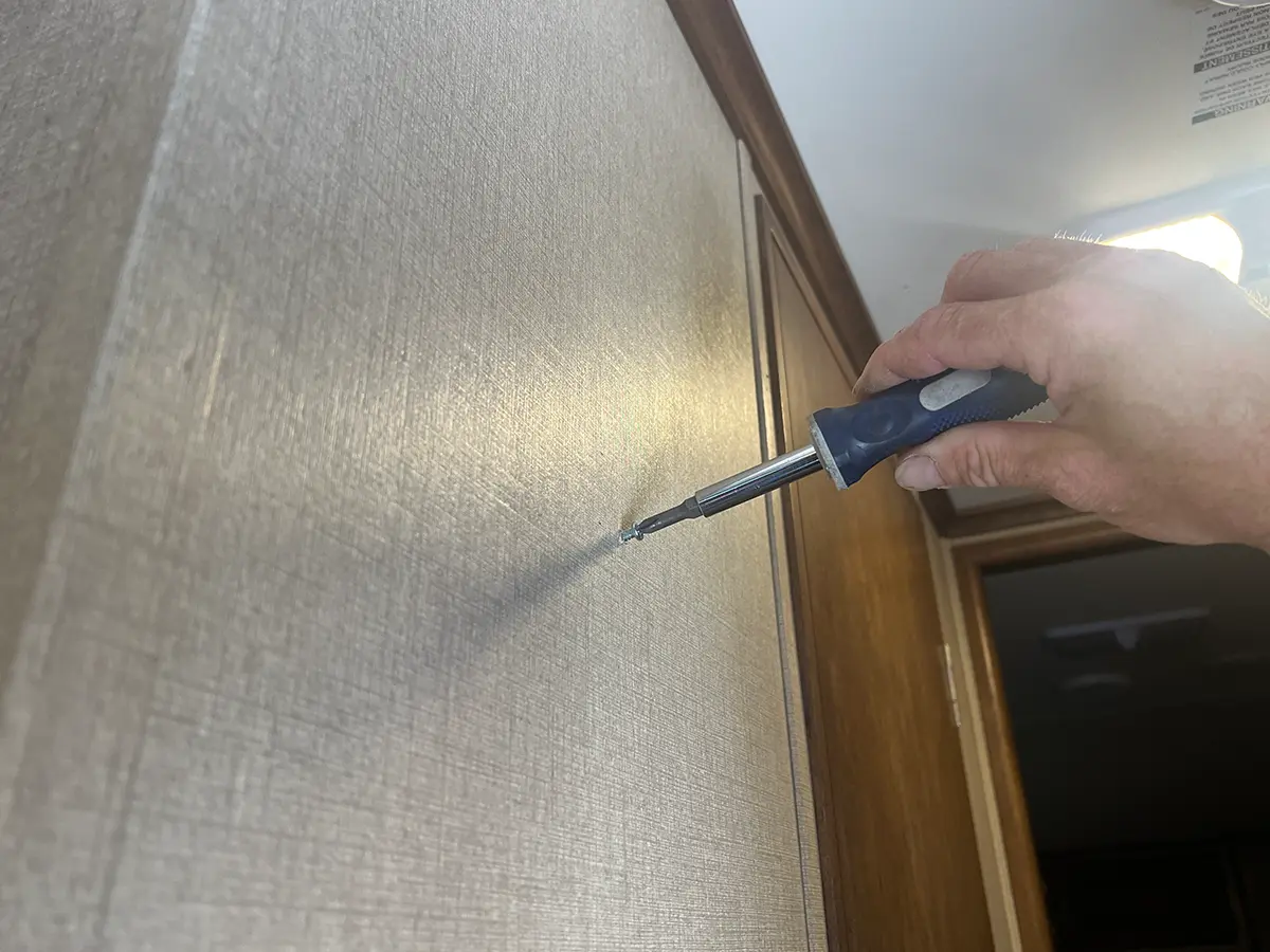 a hand inserts a single screw into an RV wall using a screwdriver