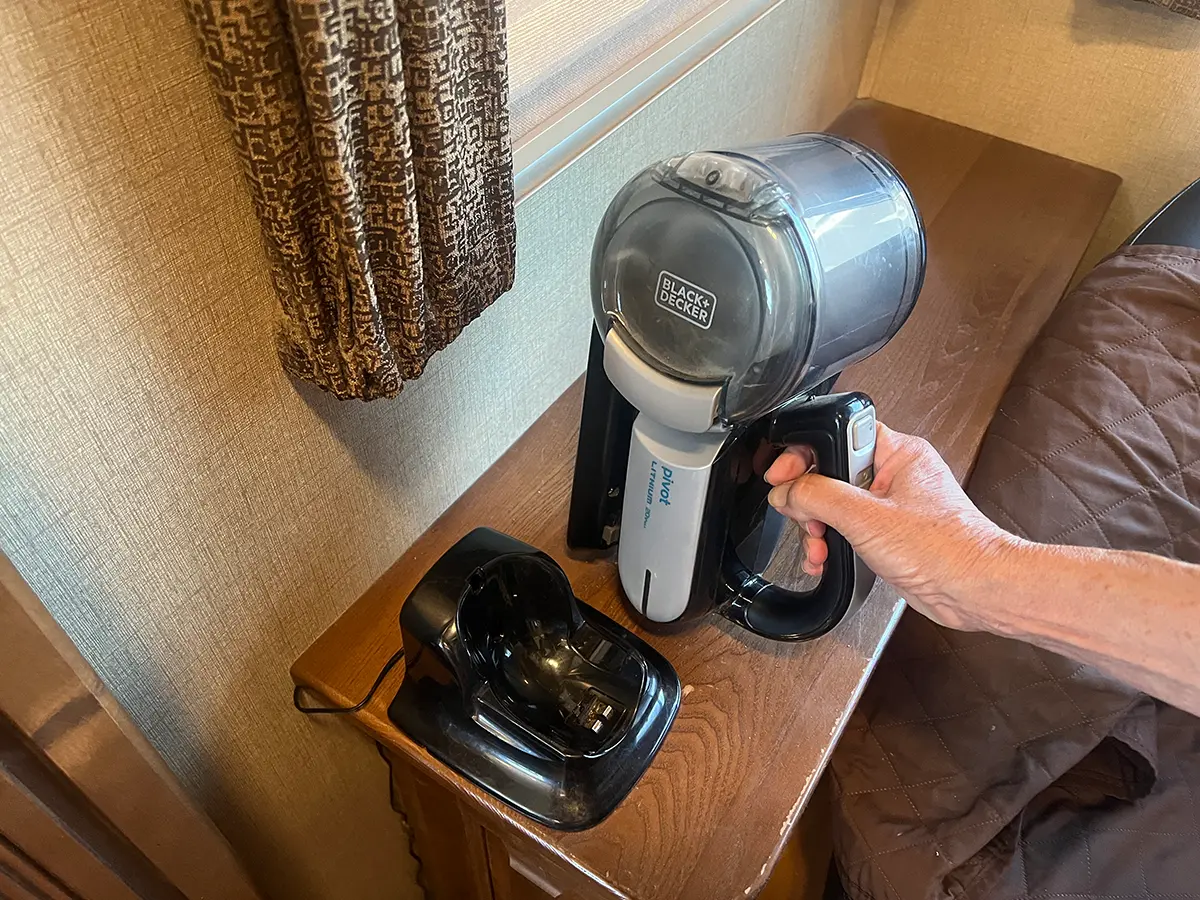 a hand holds a small vaccum beside its charging base which is mounted to a cabinet top using Alien Tape