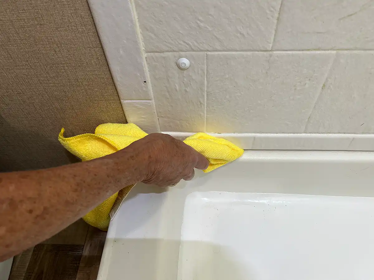 a bamboo chopstick wrapped in a microfiber towel is used to clean a seam between the shower pan and sidewalls